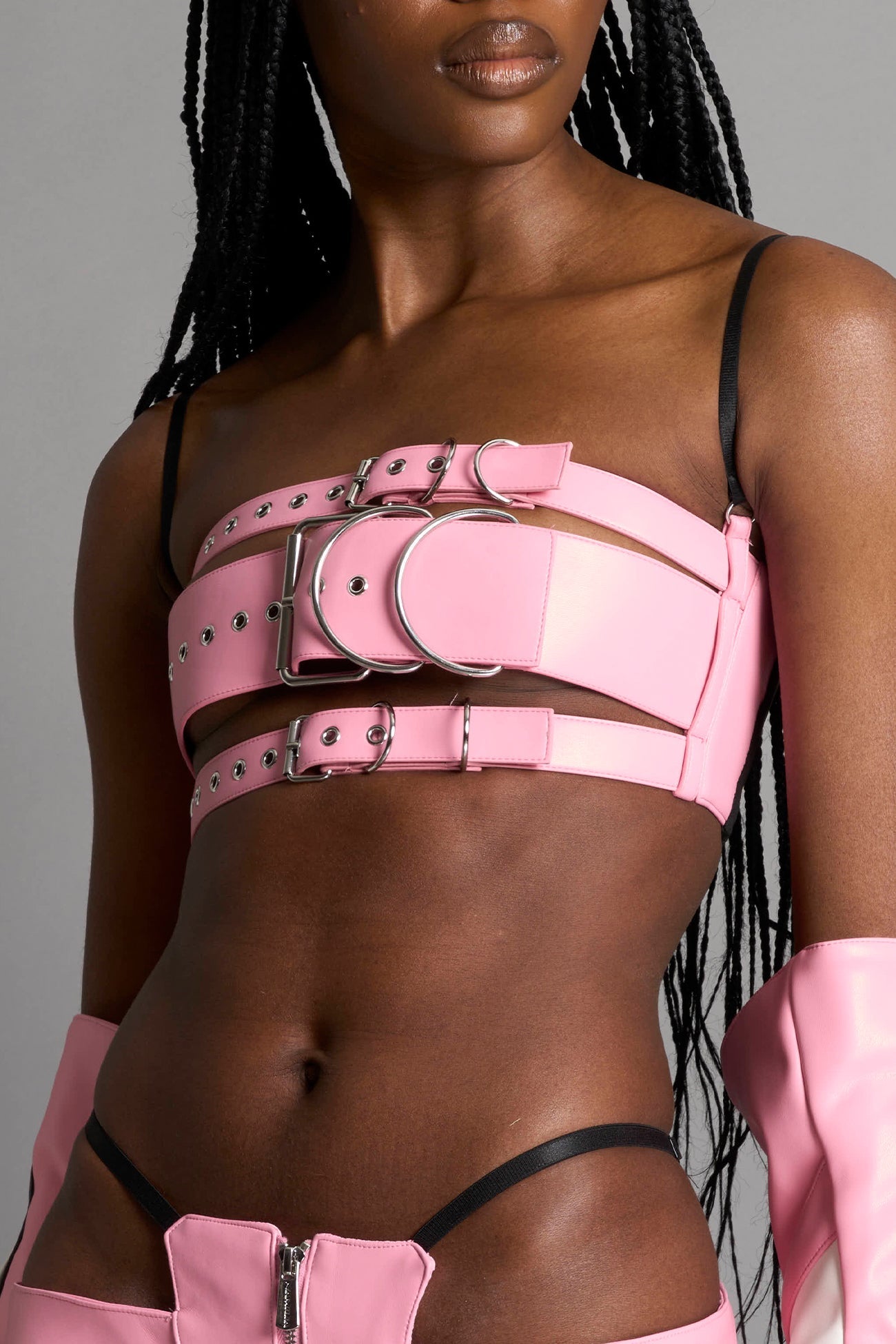 pink vegan leather belt top with three adjustable grommet straps, oversized metal buckles, and circular hardware – edgy bondage-inspired crop top for festival or clubwear.