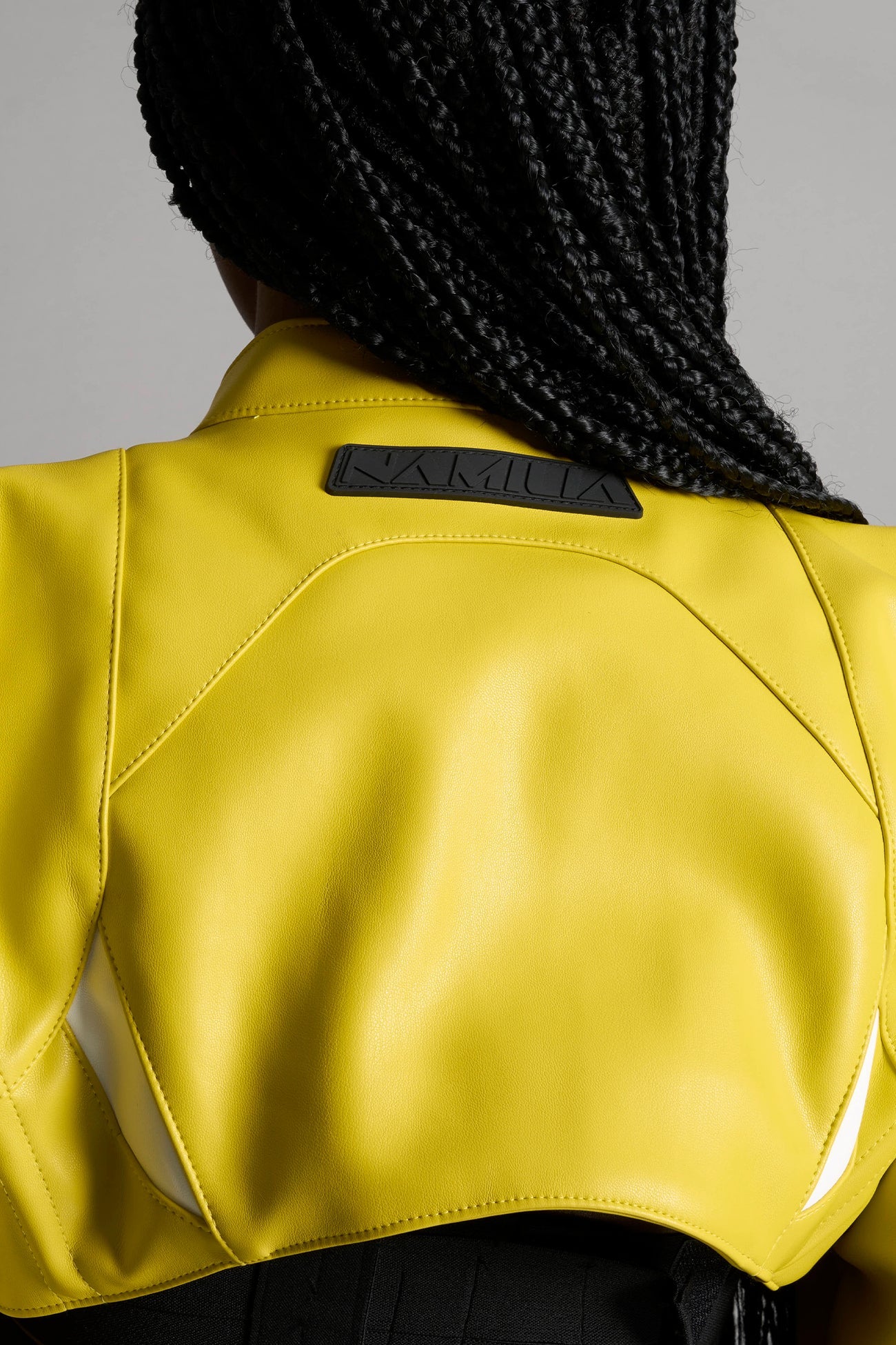 Model wears the yellow Namilia Spike Moto Bolero Jacket with wire shoulder pads, cropped hemline, branded front zipper, motocross-style lines, and black rubber logo tag on the back.