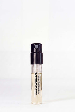 A small clear glass perfume sample vial with a black spray cap, containing a pale yellow liquid. The vial is printed with the text 'NAMILIA