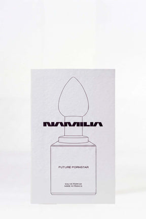 A minimalist white rectangular card or box featuring a simple black line drawing of a perfume bottle with the word 'NAMILIA' across the center and the text 'FUTURE PORNOSTAR' below, photographed against a white background.