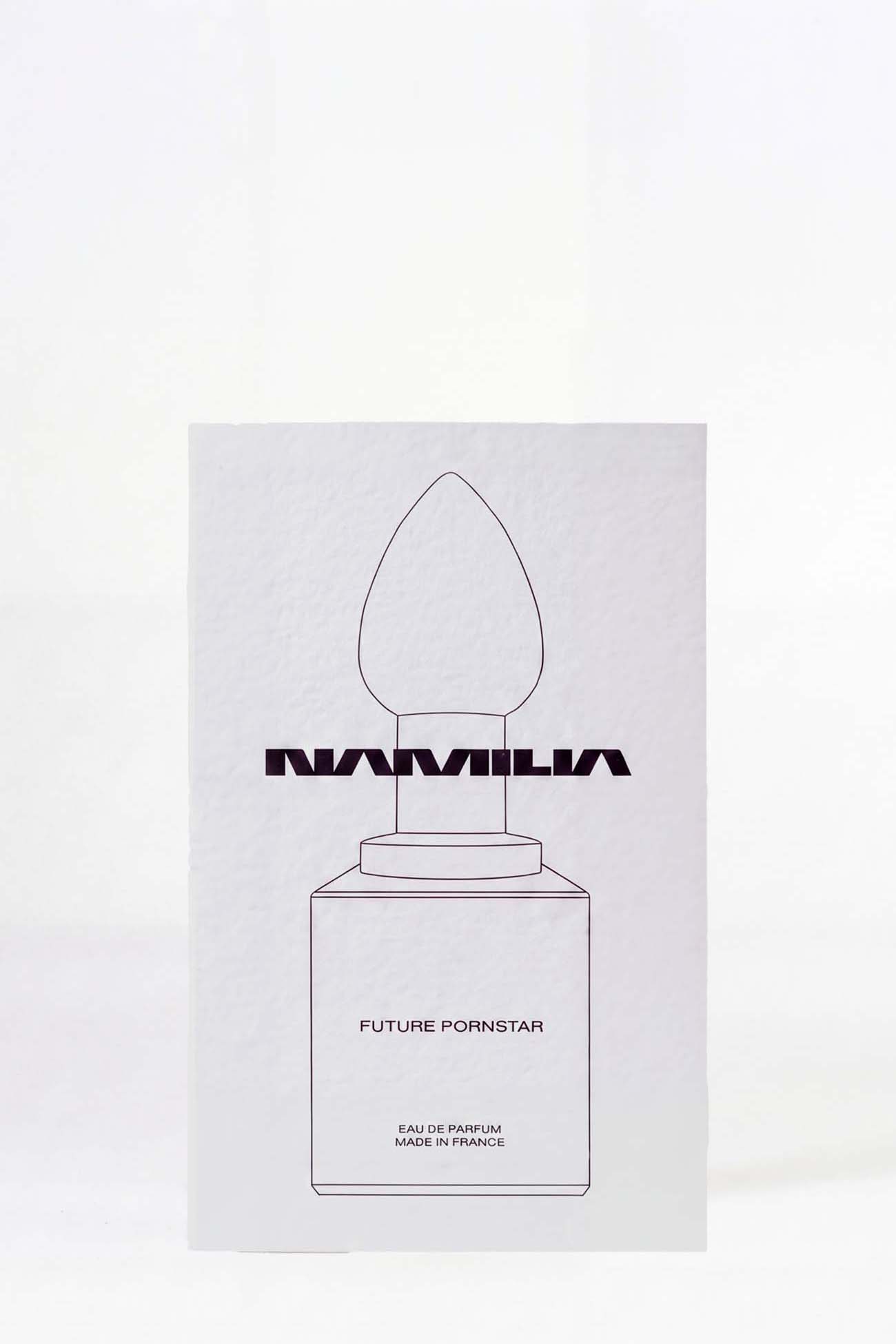 A minimalist white rectangular card or box featuring a simple black line drawing of a perfume bottle with the word 'NAMILIA' across the center and the text 'FUTURE PORNOSTAR' below, photographed against a white background.