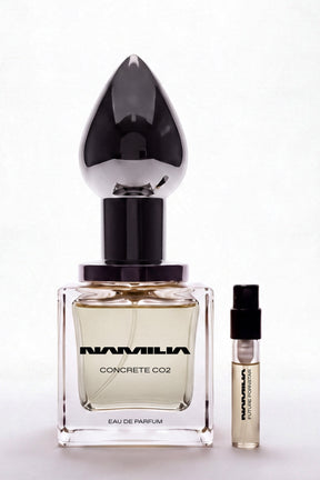 A bottle of Namila Concrete CO2 Eau de Parfum with a large reflective black teardrop-shaped cap, shown next to a small matching sample vial on a clean white background.