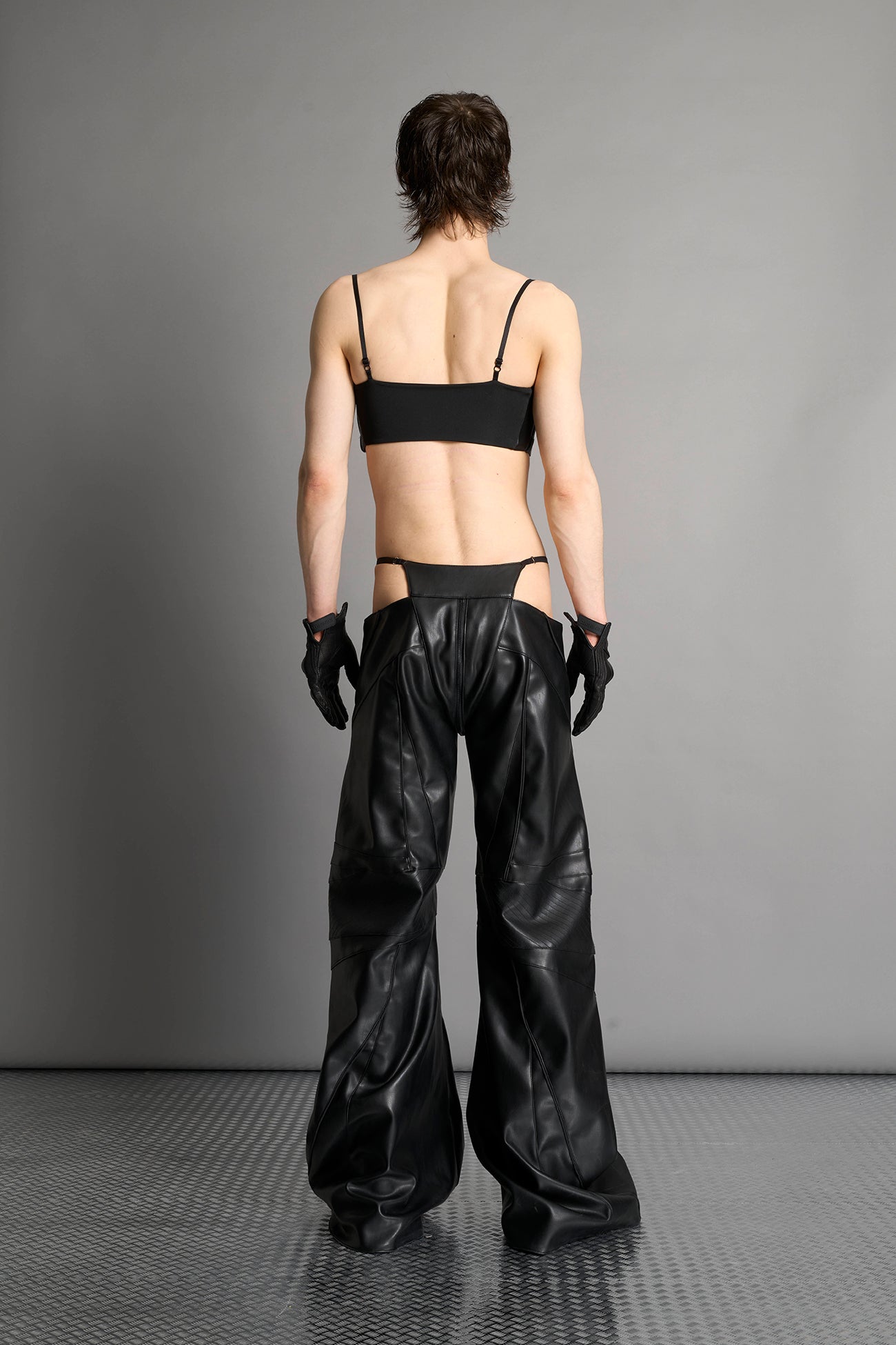 Black vegan leather belt top with three adjustable grommet straps, oversized metal buckles, and circular hardware – edgy bondage-inspired crop top for festival or clubwear.

