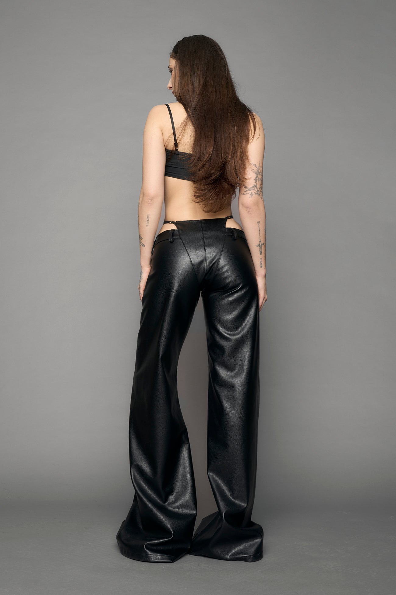 model wearing black vegan leather denim thong pants with belt detail