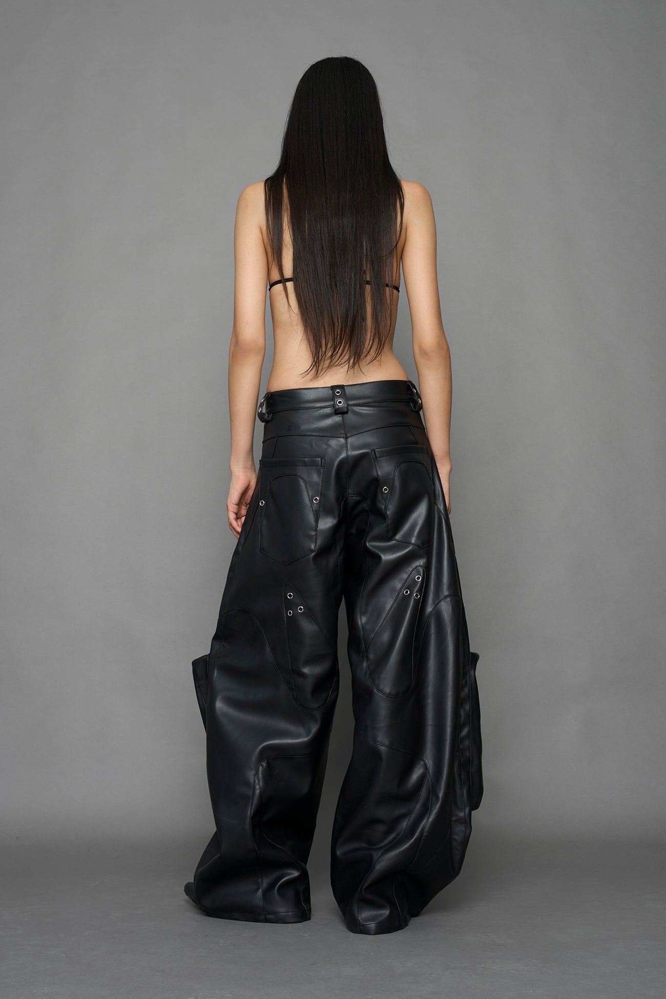 model wearing black vegan leather oversize baggy pants with pocket design details and style lines