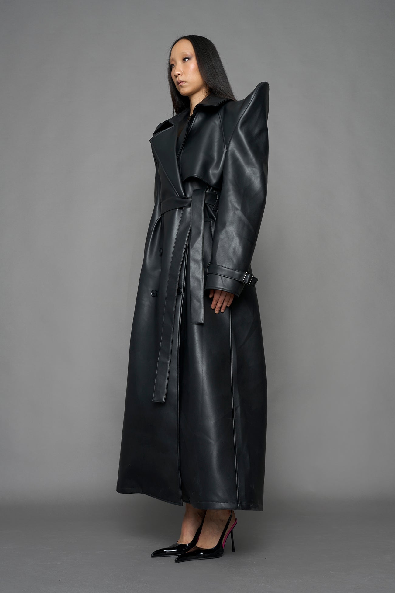model wearing black vegan leather trench coat with sharp shoulder detail 