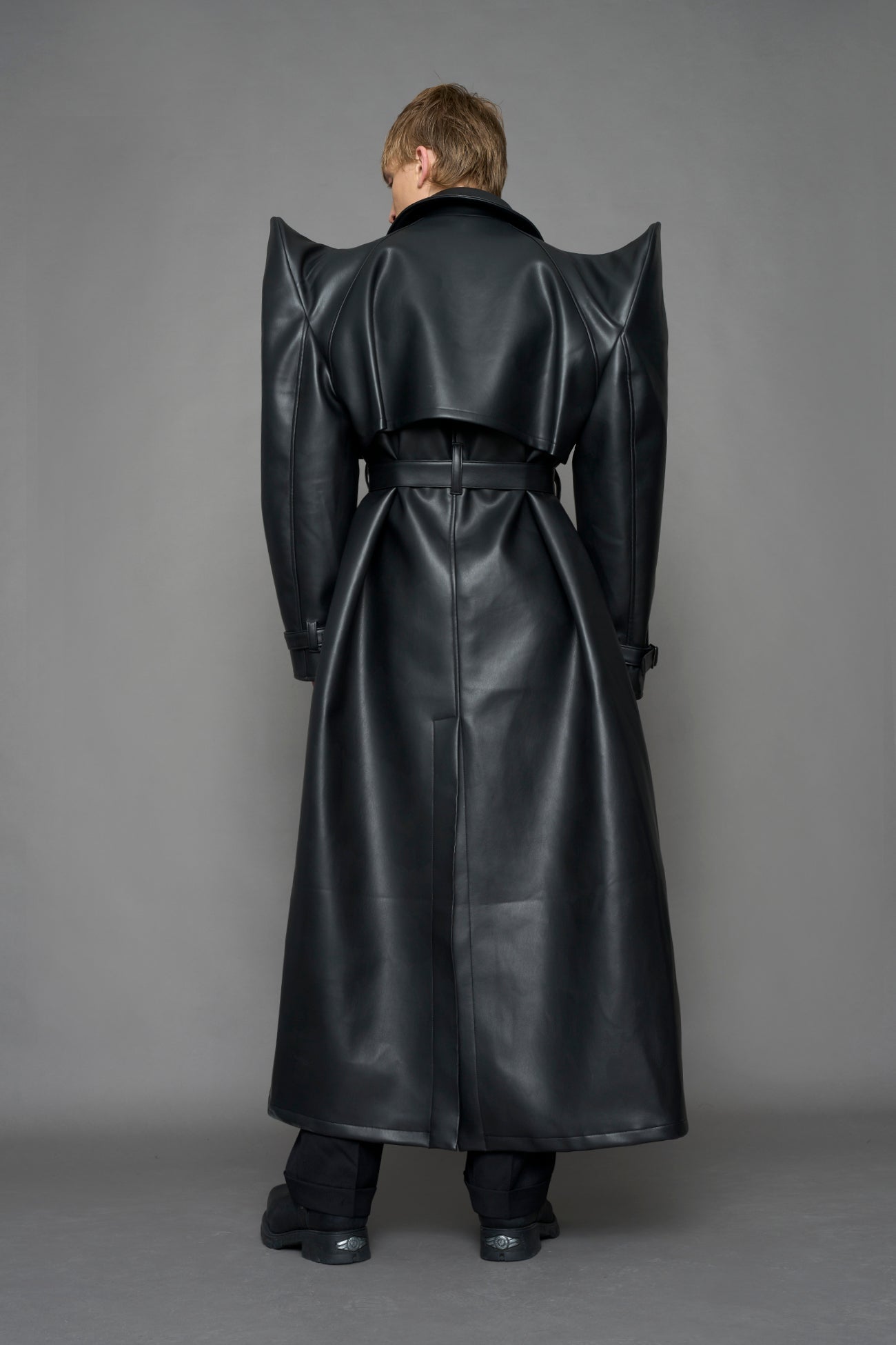 model wearing black vegan leather trench coat with sharp shoulder detail 