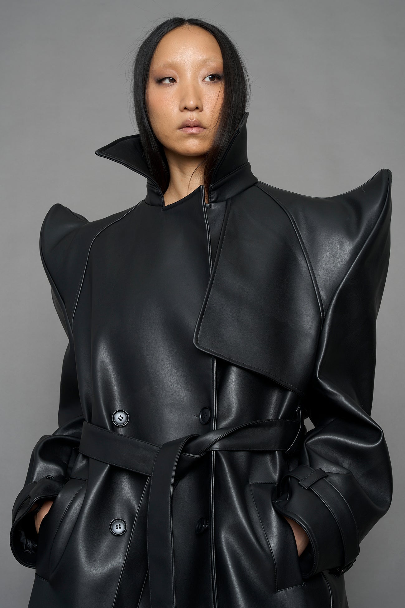 model wearing black vegan leather trench coat with sharp shoulder detail 