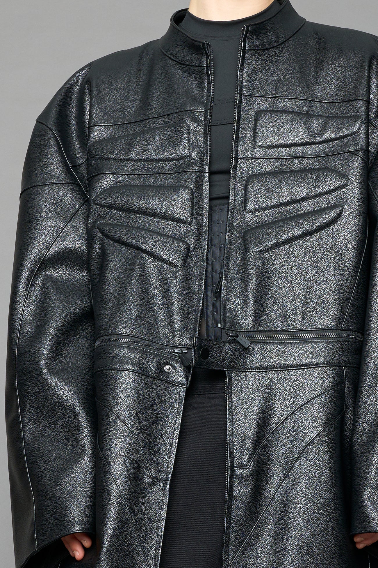 Detachable moto long coat in black vegan black leather inspired by a deconstructed full-body motocross racing suit, featuring padded panel details and a detachable zip design for two-way wear.