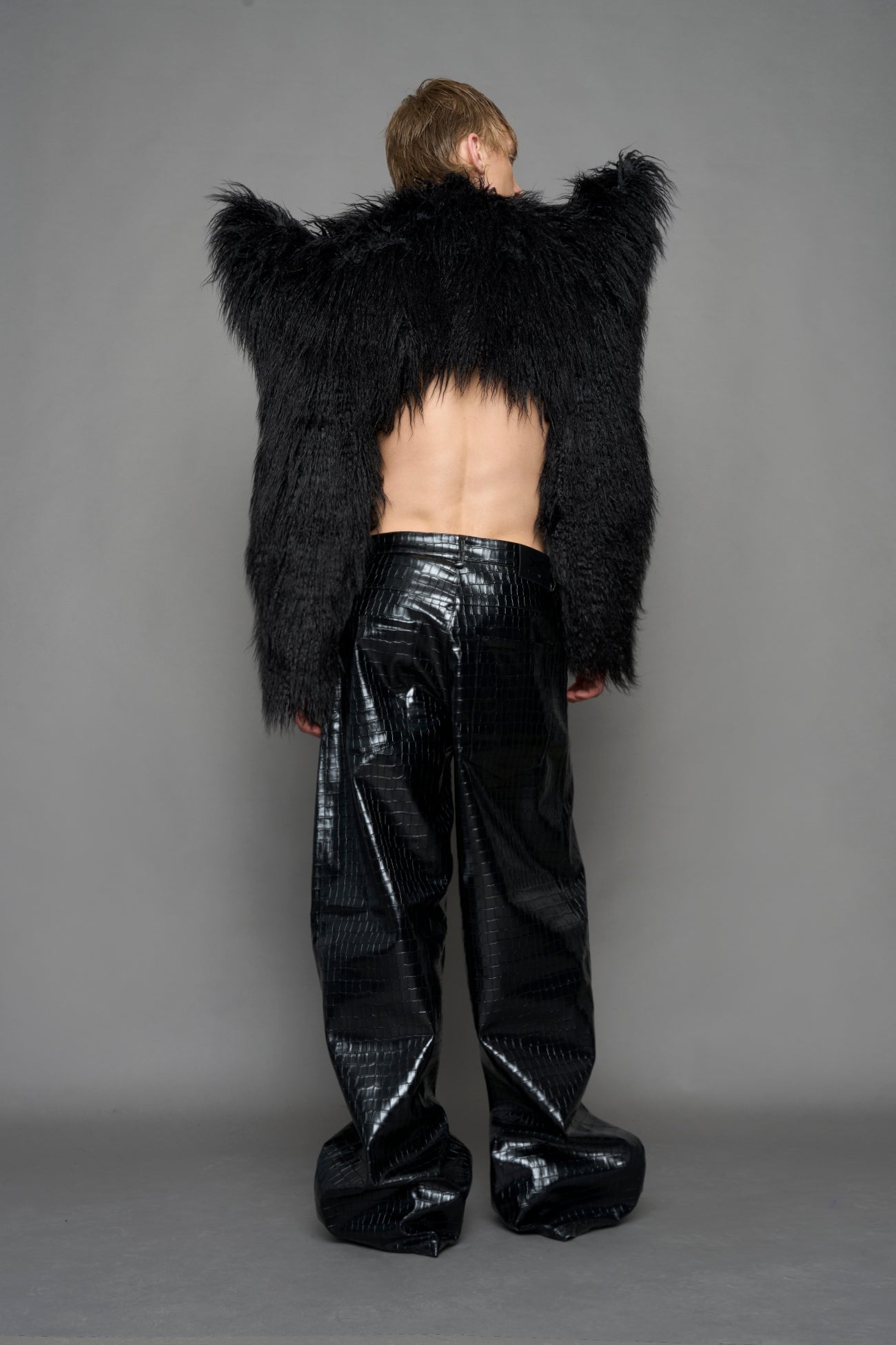 model wearing black faux fur crop jacket with sharp shoulder design and black pants