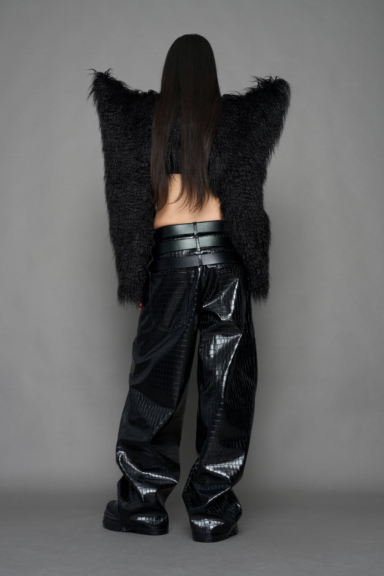 model wearing black faux fur crop jacket with sharp shoulder design and black pants