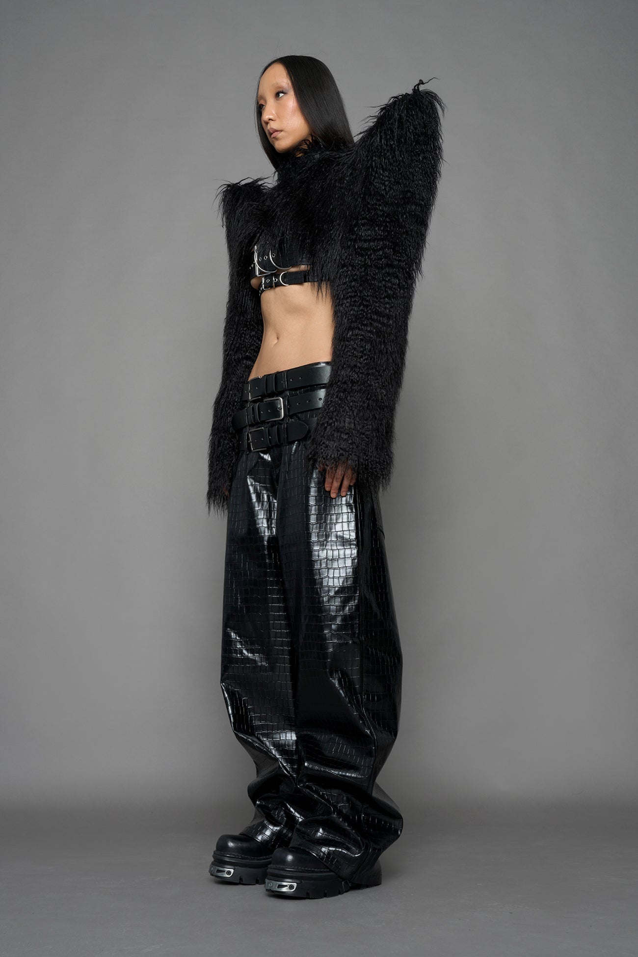 model wearing black faux fur crop jacket with sharp shoulder design and black pants