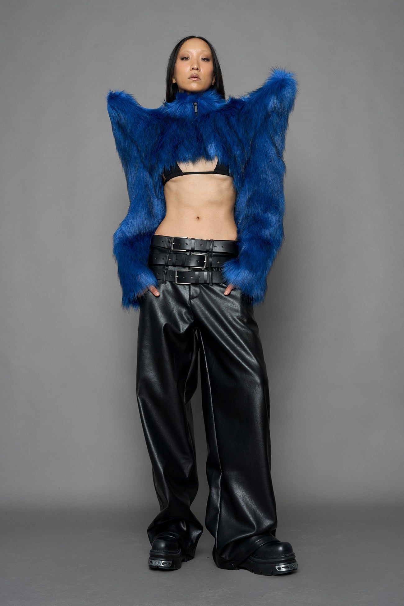 model wearing blue faux fur crop jacket with sharp shoulder design and black pants