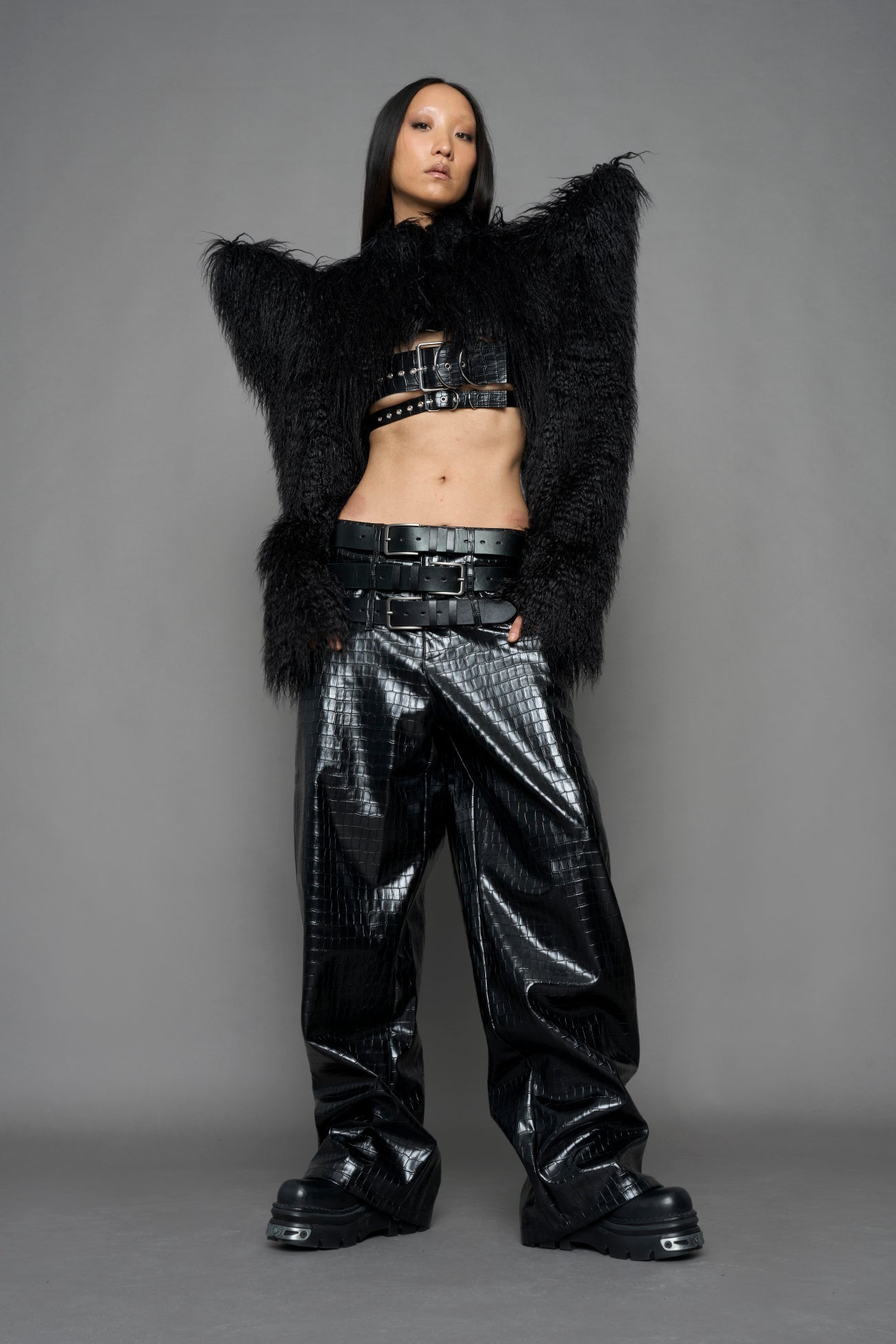 model wearing black faux fur crop jacket with sharp shoulder design and black pants