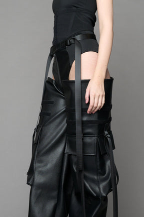 Model wearing Black vegan leather panty trousers featuring an integrated stretch panel for comfort, adjustable belt detail, and a relaxed high-waist silhouette.