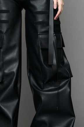 Model wearing Black vegan leather panty trousers featuring an integrated stretch panel for comfort, adjustable belt detail, and a relaxed high-waist silhouette.