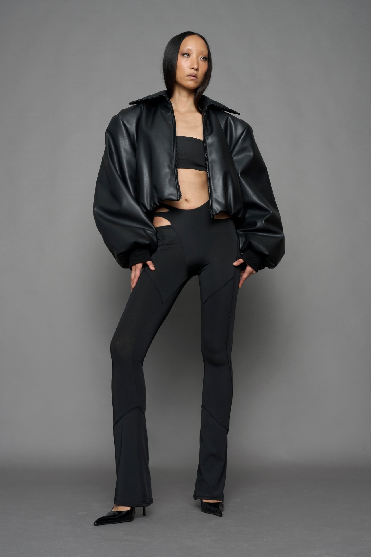 model wearing black puffy faux leather jacket with sharp collar and black pants 