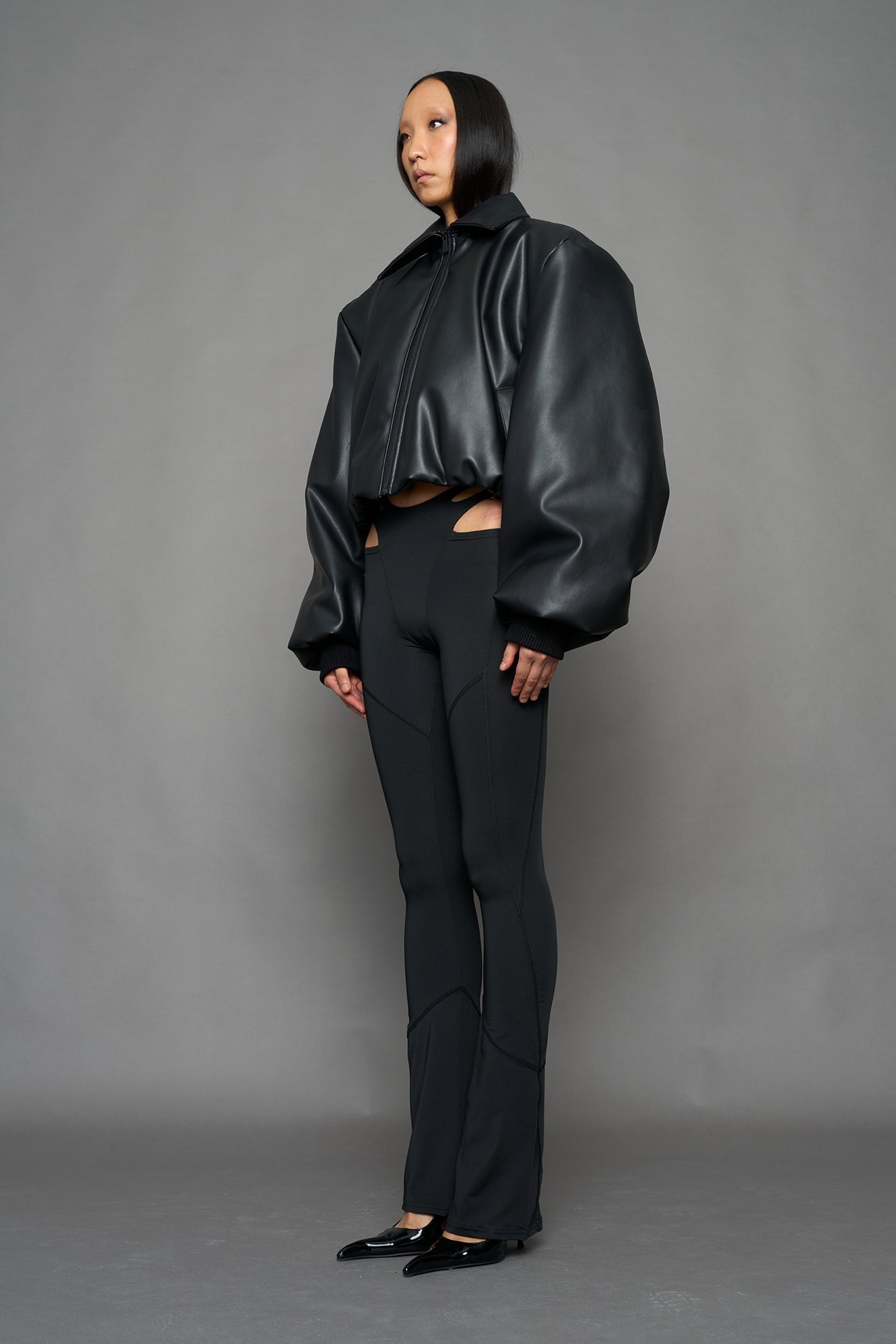 model wearing black puffy faux leather jacket with sharp collar and black pants 