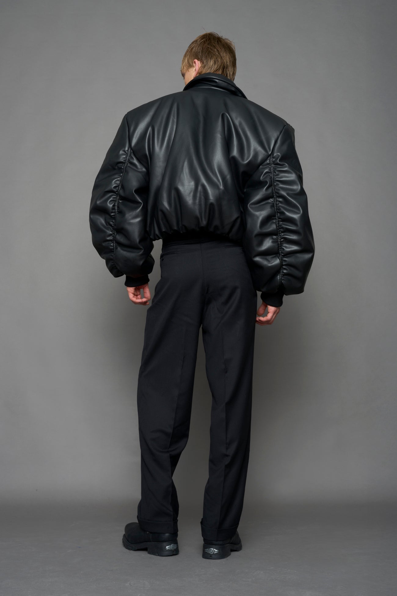 model wearing black puffy faux leather jacket with sharp collar and black pants 
