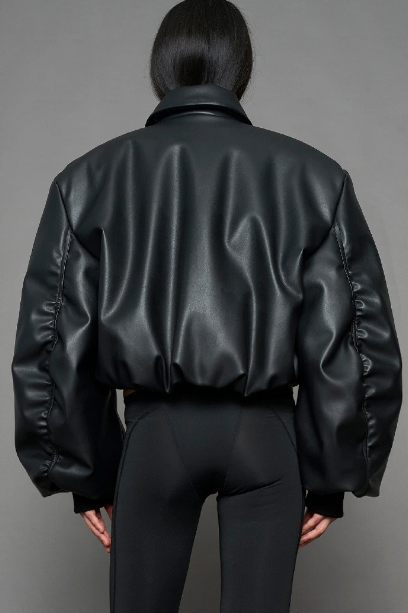 model wearing black puffy faux leather jacket with sharp collar and black pants 