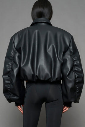 model wearing black puffy faux leather jacket with sharp collar and black pants 