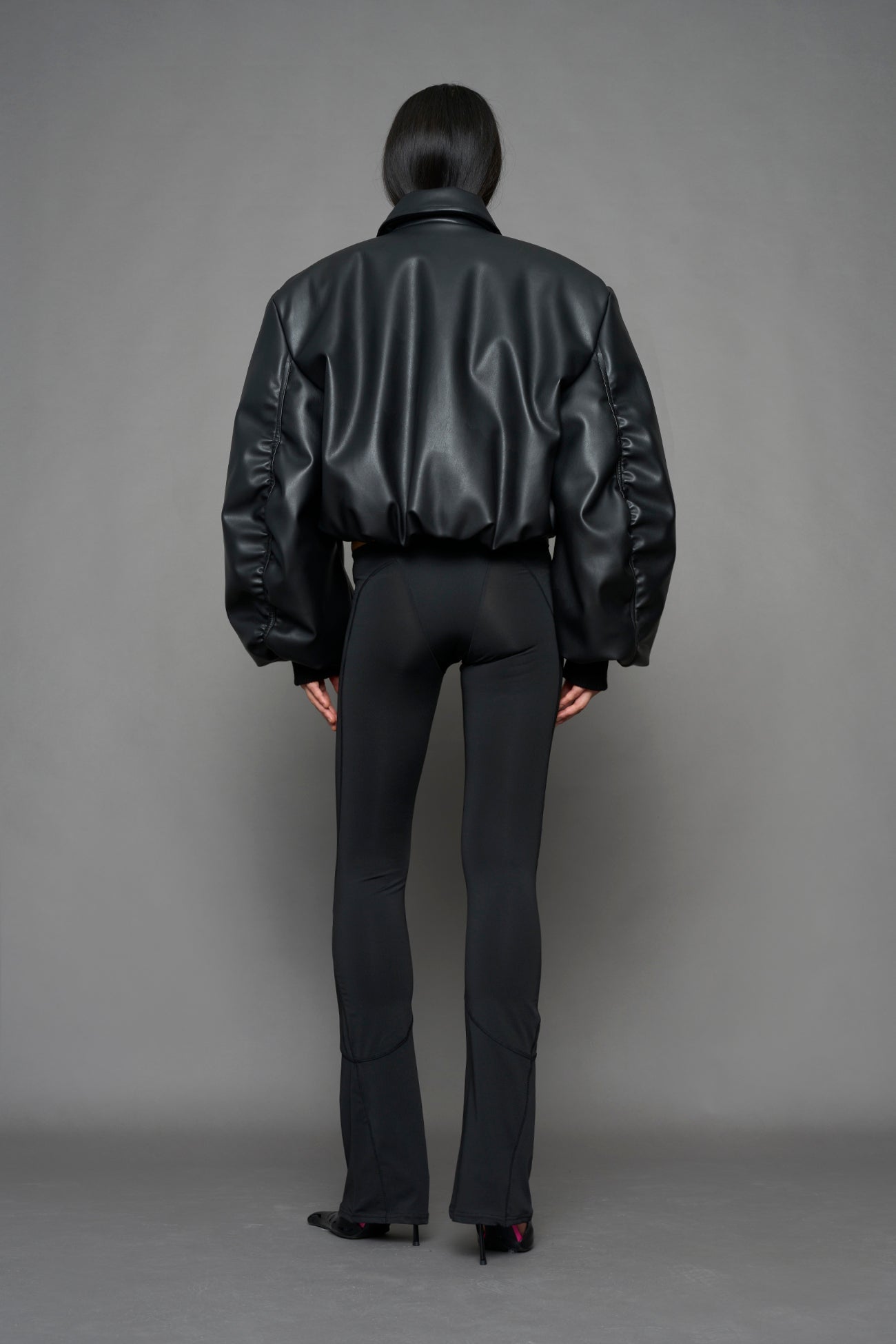 model wearing black puffy faux leather jacket with sharp collar and black pants 