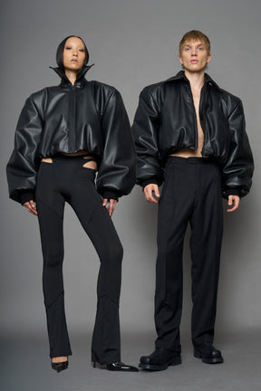 model wearing black puffy faux leather jacket with sharp collar and black pants 