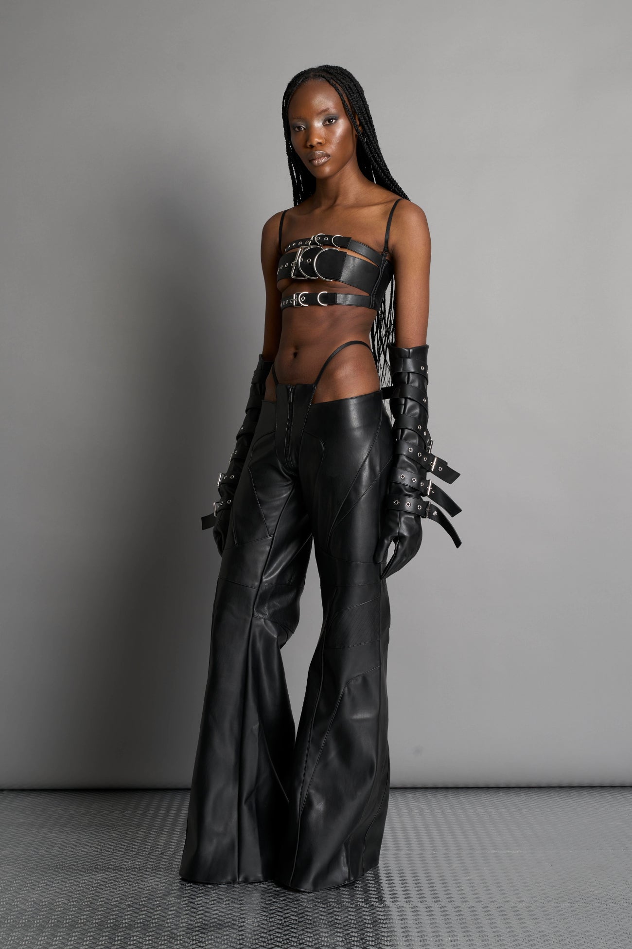 Black vegan leather belt top with three adjustable grommet straps, oversized metal buckles, and circular hardware – edgy bondage-inspired crop top for festival or clubwear.

