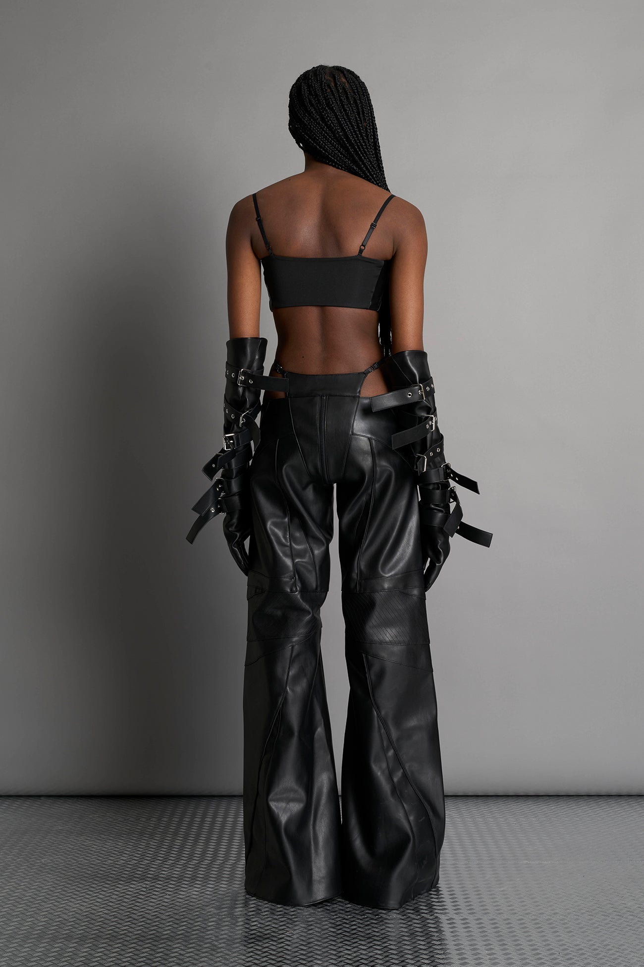 Black vegan leather belt top with three adjustable grommet straps, oversized metal buckles, and circular hardware – edgy bondage-inspired crop top for festival or clubwear.

