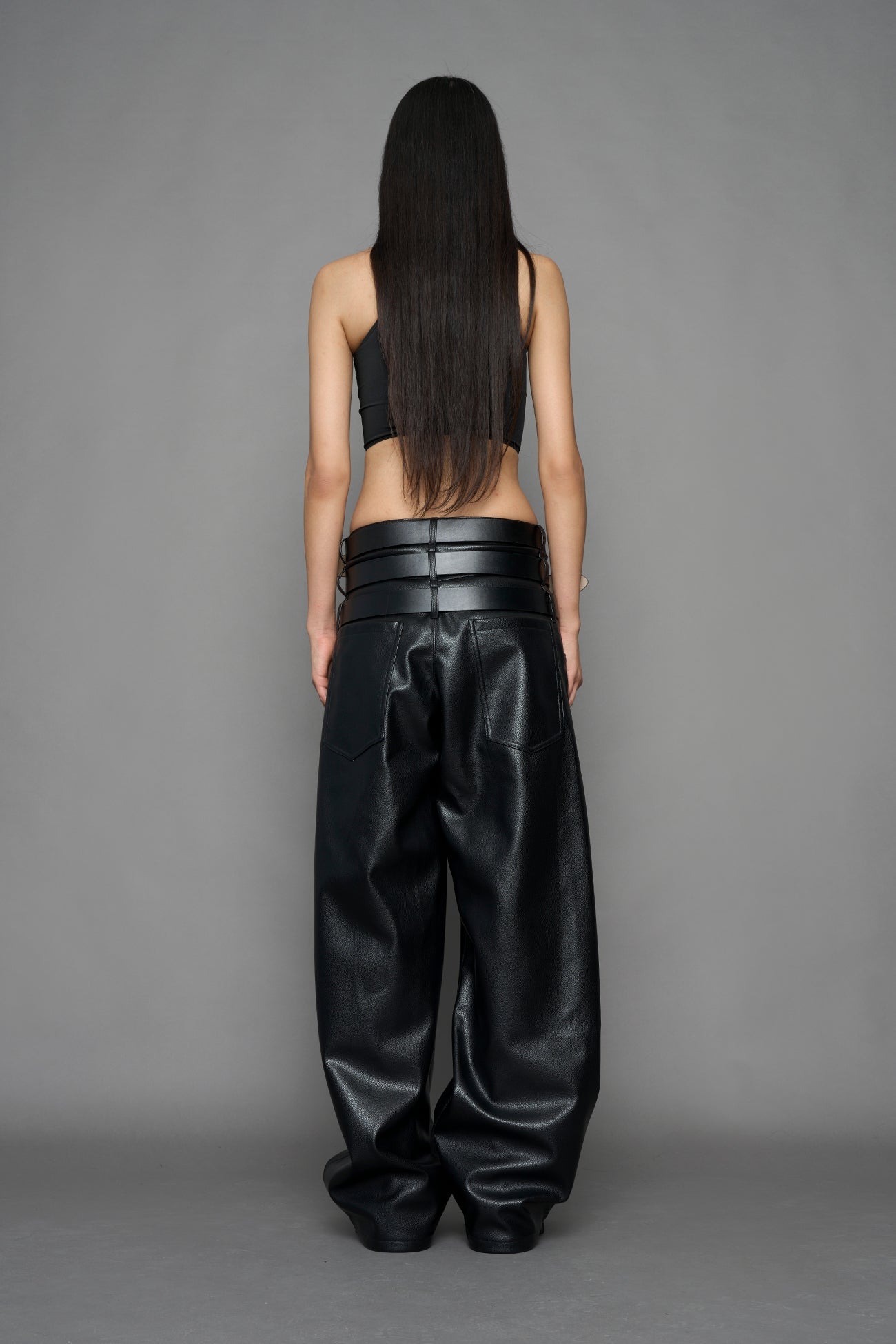 model wearing black vegan leather smooth optic baggy pants with triple belt design detail