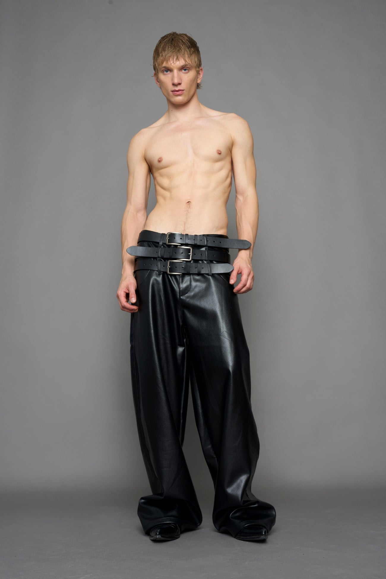 model wearing black vegan leather smooth optic baggy pants with triple belt design detail