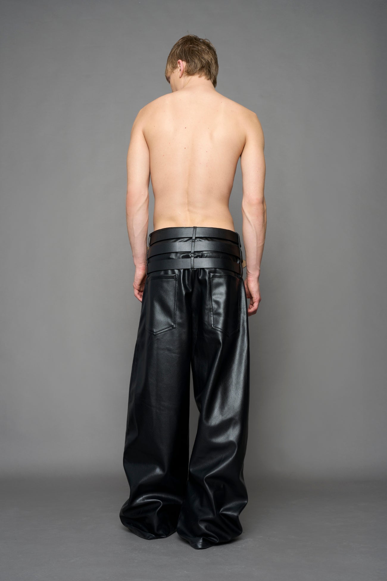 model wearing black vegan leather smooth optic baggy pants with triple belt design detail