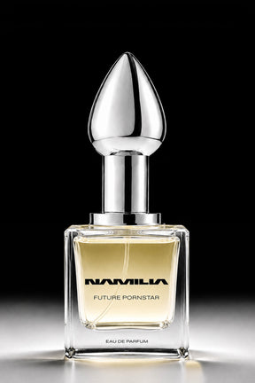A square glass perfume bottle with pale yellow liquid, a reflective silver neck, and a teardrop-shaped silver cap, centered on a black background. The bottle is labeled 'NAMILIA FUTURE Pornstar EAU DE PARFUM'.