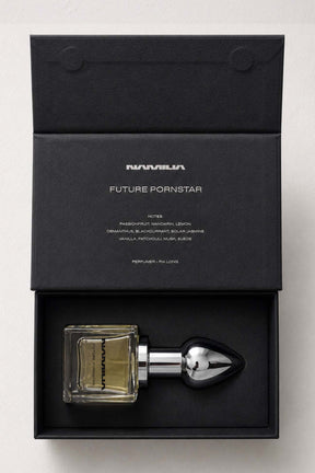 A perfume bottle with a black Plug-shaped atomizer and a square glass bottle filled with amber liquid, presented in an open black box. The box lid is printed with the brand name 'NAMILIA' and the scent name 'FUTURE PORNSTAR'.