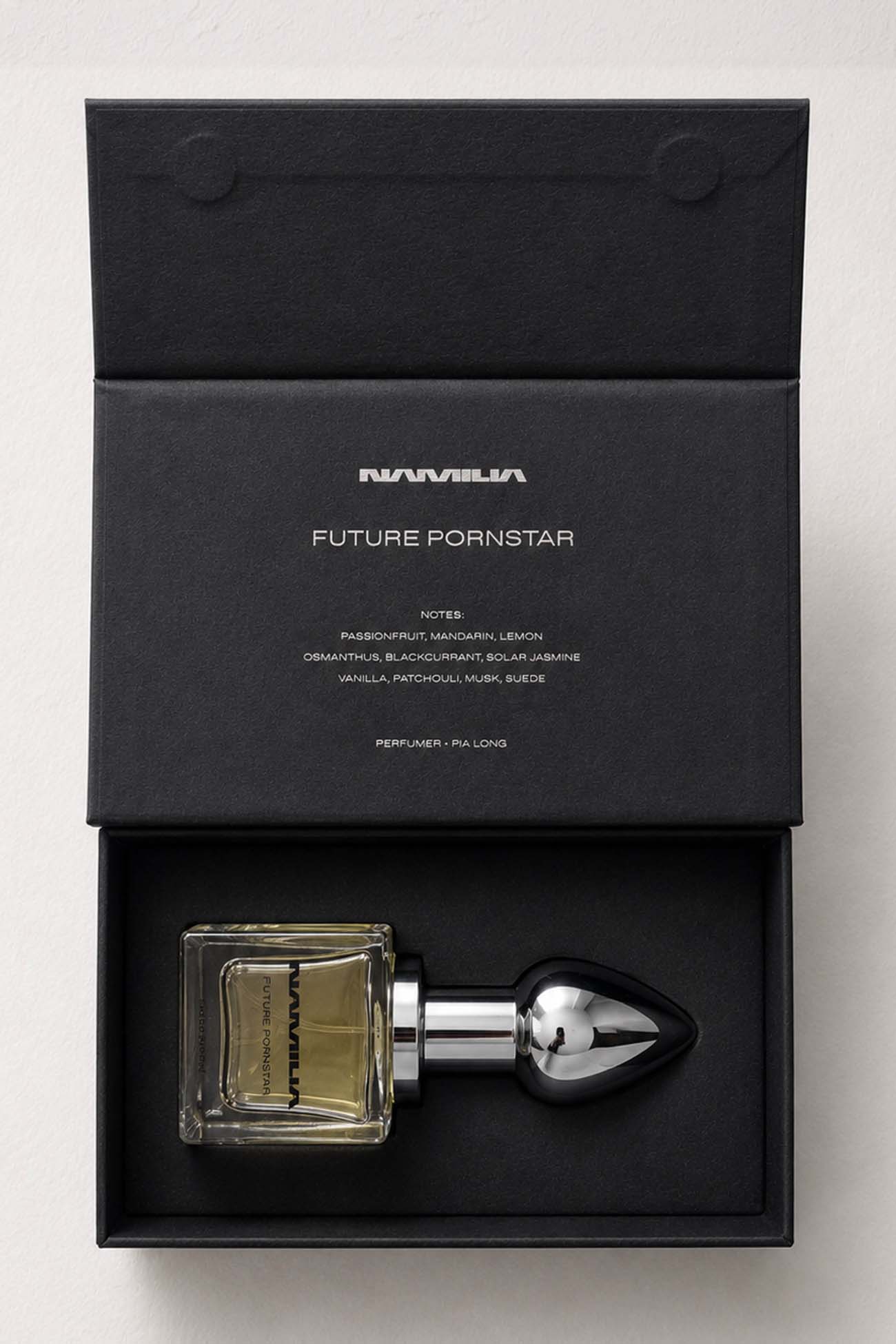 A perfume bottle with a black teardrop-shaped atomizer and a square glass bottle filled with amber liquid, presented in an open black box. The box lid is printed with the brand name 'NANUMIA' and the scent name 'FUTURE PORNSTAR'.