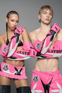 Two models posing in matching pink and black Playboy bunny lingerie sets with oversized pink gloves, against a solid gray studio background.